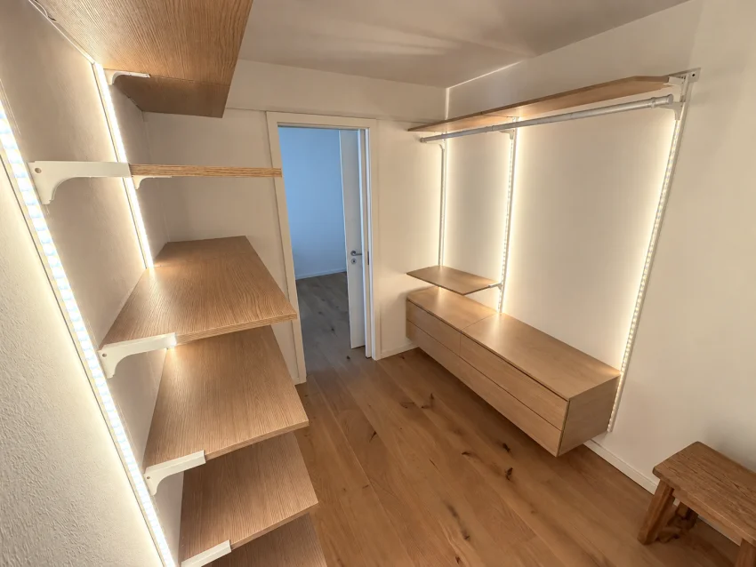Empty dressing room with wooden shelves, clothes rails, drawers and lighting