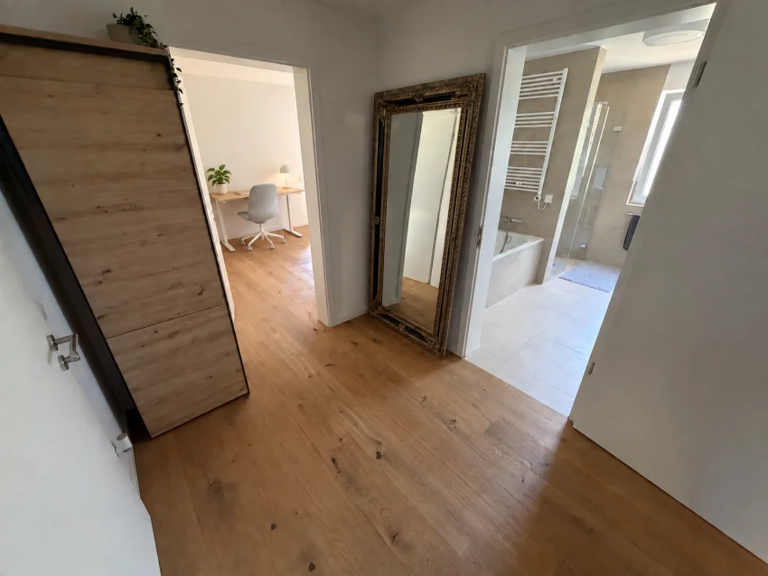 Hallway with wardrobe and mirror, looking towards the desk with a light-grey chair and the bathroom