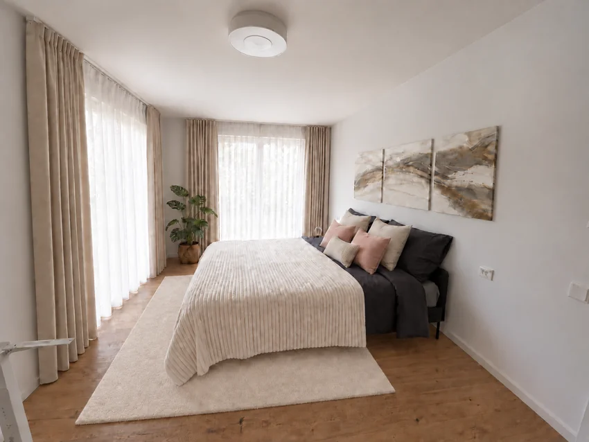 Bright bedroom with cream-coloured textiles and curtains at two French doors