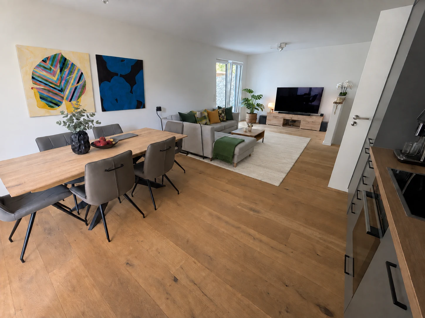Open-plan living and dining area with parquet flooring, a wooden dining table and a generous sofa